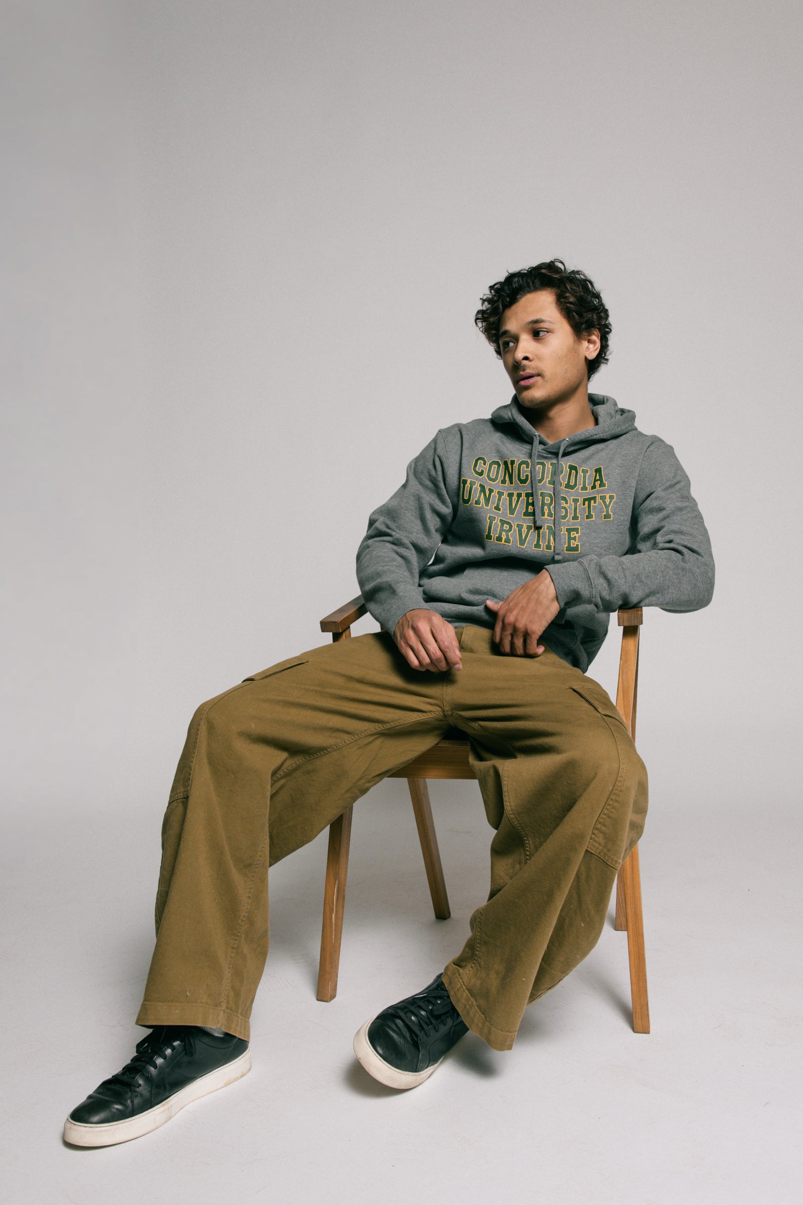 Person wearing a gray hoodie with text, sitting on a chair against a plain background