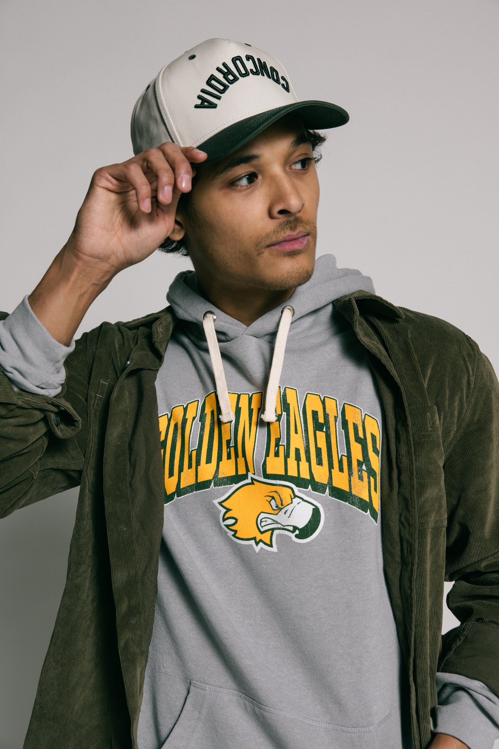 Person wearing a gray hoodie with 'Golden Eagles' text and logo, holding a cap.
